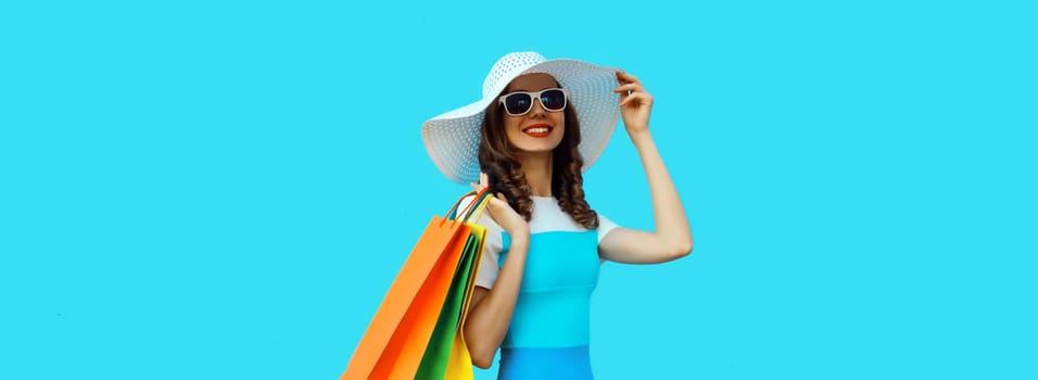 Stylish beautiful happy smiling young woman posing with bright colorful shopping bags wearing summer straw hat on blue background