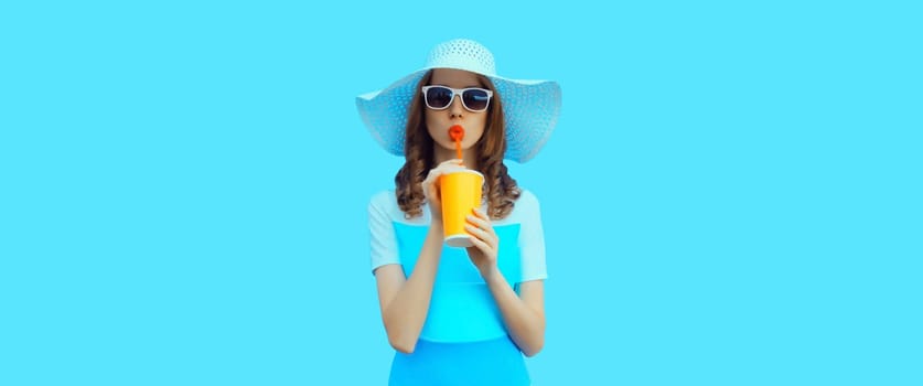 Summer portrait of beautiful caucasian young woman with cup of coffee or fresh juice wearing white straw hat on studio blue background