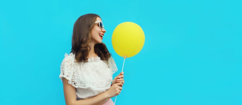 Summer portrait of happy pretty young woman with yellow balloon on blue studio background