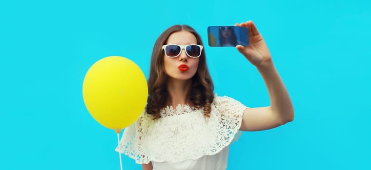 Portrait of beautiful young woman 20s taking selfie with smartphone and blowing her lips sends kiss on blue studio background