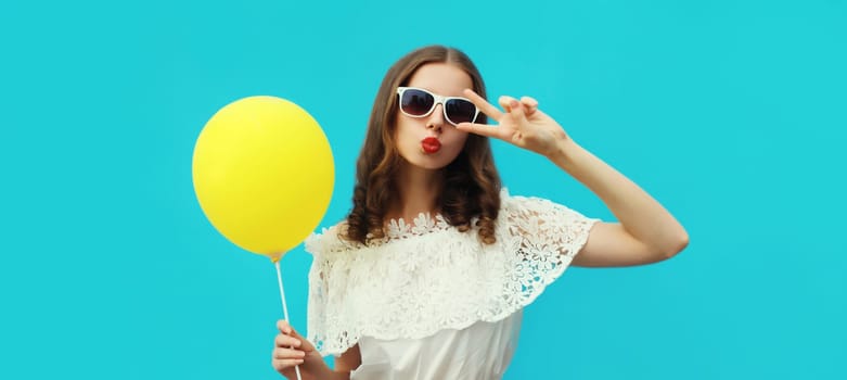 Summer portrait of happy pretty young woman with yellow balloon on blue studio background