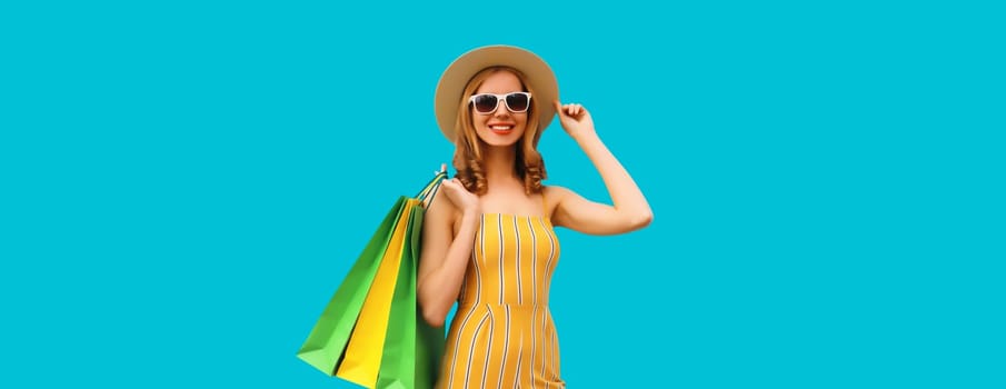 Stylish beautiful happy smiling young woman posing with bright colorful shopping bags wearing summer straw hat on blue background