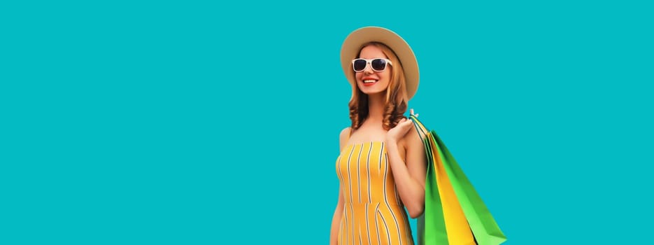 Stylish beautiful happy smiling young woman posing with bright colorful shopping bags wearing summer straw hat on blue background