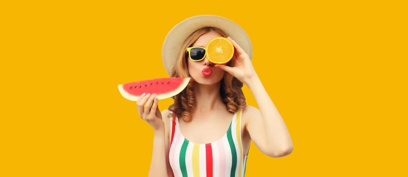 Summer portrait of happy young woman with fresh juicy fruits, slice of watermelon wearing straw hat, glasses and blowing kiss on bright yellow background