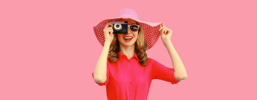 Summer portrait of happy smiling young woman photographer with film camera wearing straw hat, pink dress, sunglasses on background