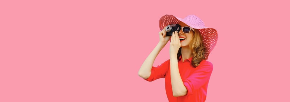 Summer portrait of happy smiling young woman photographer with film camera wearing straw hat, pink dress, sunglasses on background