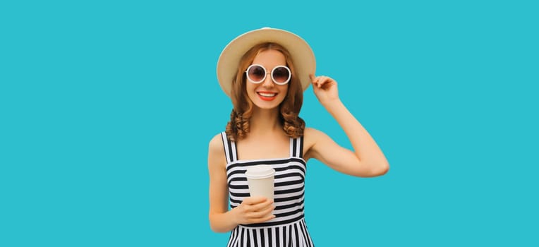 Portrait of happy smiling young woman drinking fresh juice or coffee wearing summer straw hat, striped dress on blue background