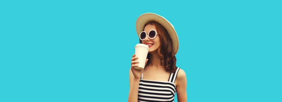 Portrait of happy smiling young woman drinking fresh juice or coffee wearing summer straw hat, striped dress on blue background