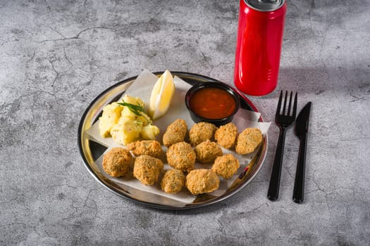 Fried mussels on a metal plate with potato salad on the side. Turkish name: Midye Tava