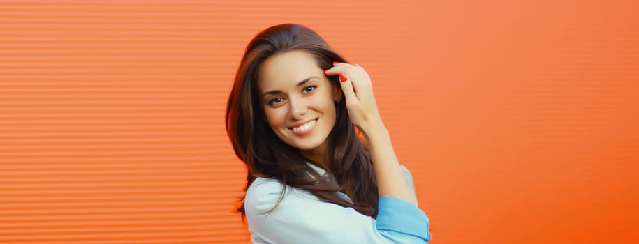 Portrait of beautiful happy smiling brunette young woman posing in the city on orange background