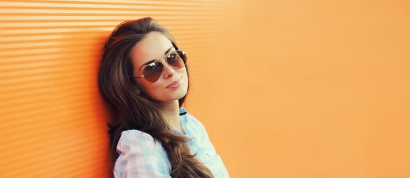 Portrait of beautiful brunette young woman in sunglasses posing in the city on orange background, copy space