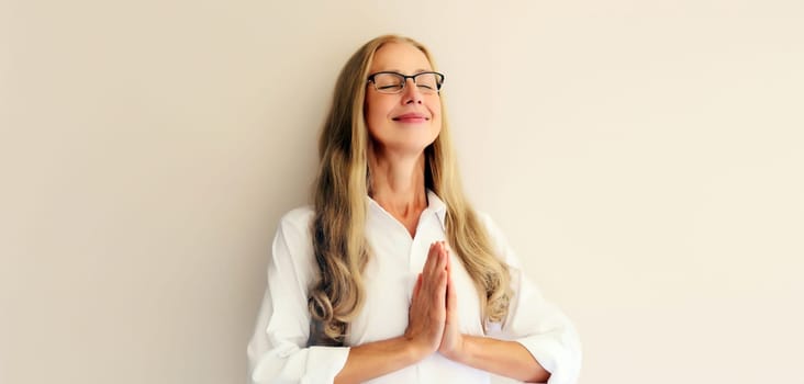 Calm relaxing healthy middle-aged woman meditates, practicing yoga on white studio background