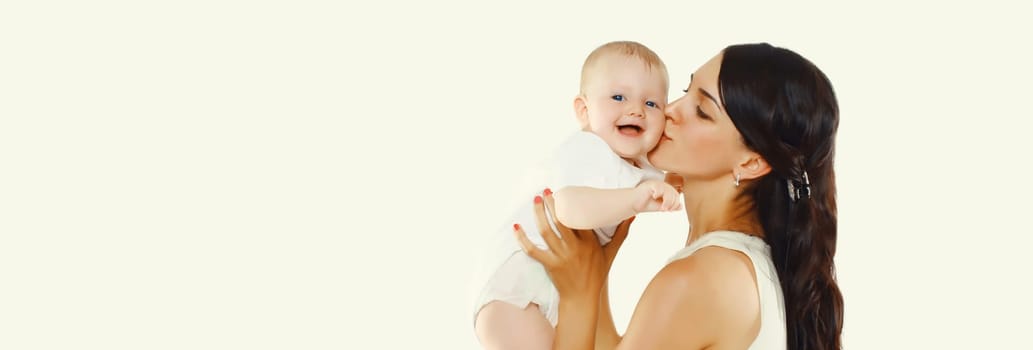 Happy young mother holding and kissing baby on white studio background