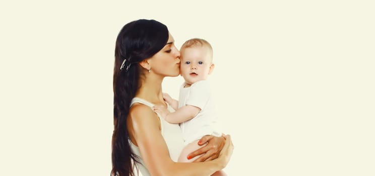 Happy young mother holding and kissing baby on white studio background