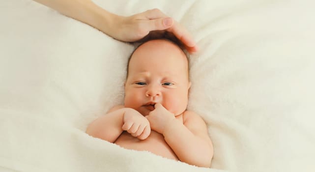 Mother hand stroking infant sweet, baby sleeping lying on white bed at home