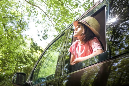 A young boy is sitting in a car window, looking out at the trees. The scene is peaceful and serene, with the boy enjoying the view and the fresh air