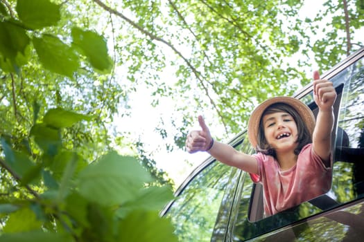 A kid is giving thumbs up from the window of a van. He is smiling and she is enjoying the ride