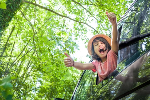 A young boy is in a van window, giving thumbs up and laughing. Concept of joy and excitement, as the boy is enjoying her time in the car