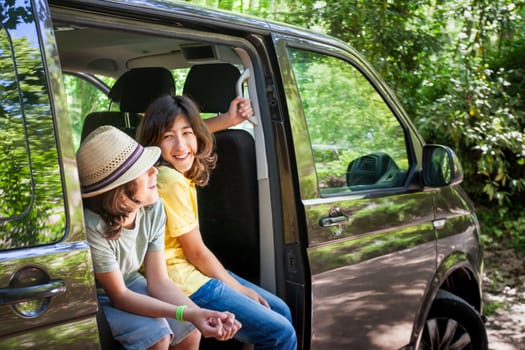 Two children are sitting in a van, one wearing a yellow shirt and the other wearing a straw hat