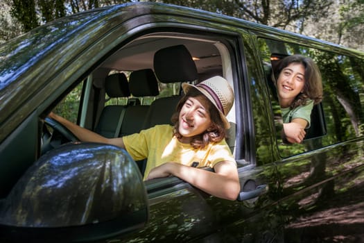 Two young boys are riding in a van, one of them is wearing a yellow T-shirt. They smile and look out of the window. One of them pretends to drive while sitting behind the wheel. 