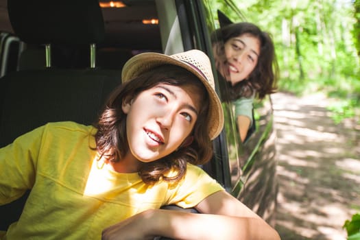 Two young men are sitting in a car, sticking their heads out of the window. They are smiling and looking out the window