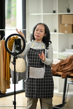 Smiling senior woman business owner presenting new collection while live streaming at her shop.