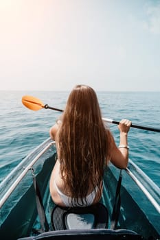 Woman in kayak back view. Happy young woman with long hair floating in transparent kayak on the crystal clear sea. Summer holiday vacation and cheerful female people having fun on the boat.