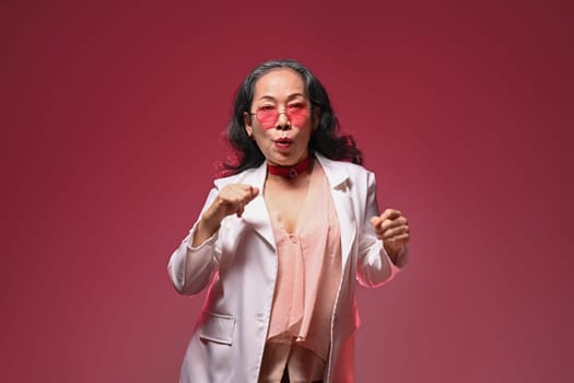 Happy and carefree middle age woman with sunglasses dancing over red background.