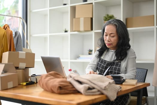 Middle age small business owner checking purchase order on laptop at her shop.