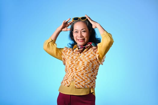 Cool and stylish asian senior woman with sunglasses and fashionable clothes on light blue background.