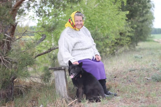 Elderly grayhaired in yellow headskarf woman with her lovely black dog in the park. She seats on a bench. High quality photo