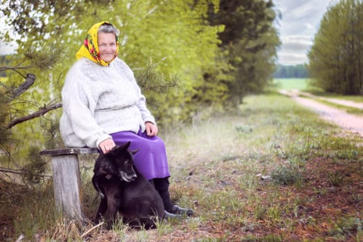 Elderly grayhaired in yellow headskarf woman with her lovely black dog in the park. She seats on a bench. High quality photo