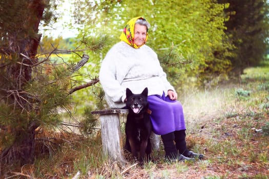 Elderly grayhaired in yellow headskarf woman with her lovely black dog in the park. She seats on a bench. High quality photo