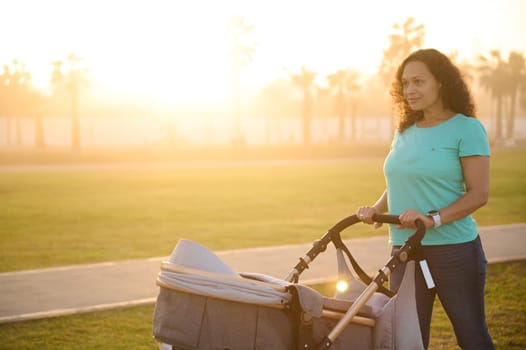 Family, infancy, babyhood and parenthood. Happy mother walking with baby stroller in park at sunset. The concept of active healthy lifestyle and breathing fresh air during daily walking outdoors.