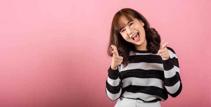 Woman excited smiling makes finger two gun gesture to camera isolated pink background, Happy Asian portrait beautiful young female says you are chosen ll kill you or what up man with cheeky copy space