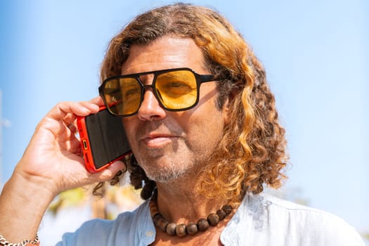 Caucasian man wearing sunglasses talks on cell phone and smiles outdoors