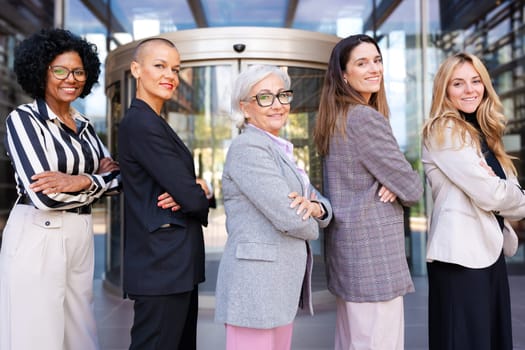 Five businesswomen standing side by side with their arms crossed looking at the camera smiling. Suitable for team, friendship and diversity concepts.