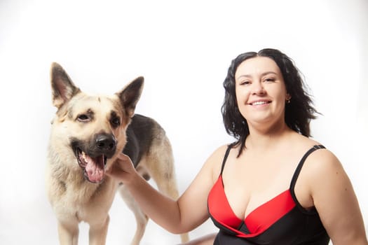 Portrait of attractive thick woman in red black swimsuit with big dog shepherd on white background. Body positive, selfie of Funny plus size model