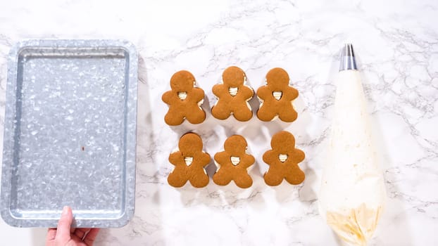 Flat lay. Gingerbread cookies await their second halves on a marble surface, each meticulously piped with buttercream to craft delightful sandwich treats. The precision of the piping adds a festive touch.