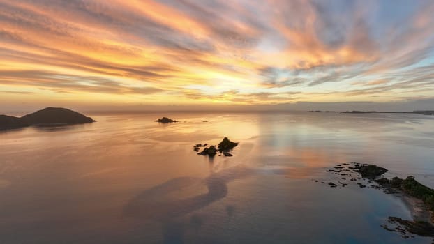 Bright orange sun rising over the beach town of Oakura, New Zealand. Silhouetted rocky islands and outlets frame the serene and tranquil scene