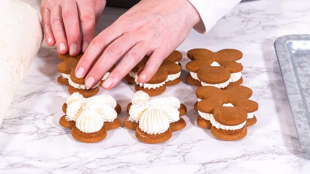 Gingerbread cookies await their second halves on a marble surface, each meticulously piped with buttercream to craft delightful sandwich treats. The precision of the piping adds a festive touch.