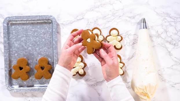 Flat lay. Gingerbread cookies await their second halves on a marble surface, each meticulously piped with buttercream to craft delightful sandwich treats. The precision of the piping adds a festive touch.