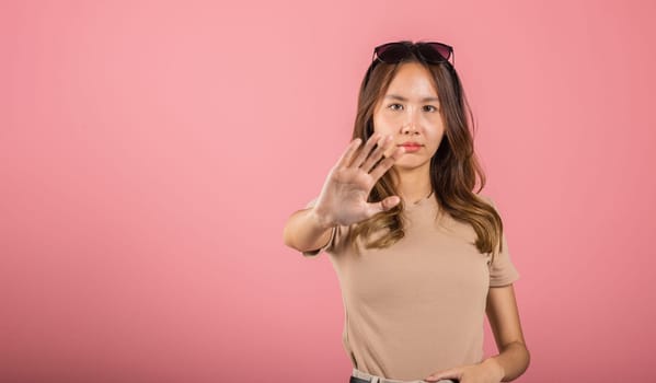 Asian beautiful woman itching her outstretched hand showing stop gesture front face on pink background with copy space, female doing show stop sign with palm of hand