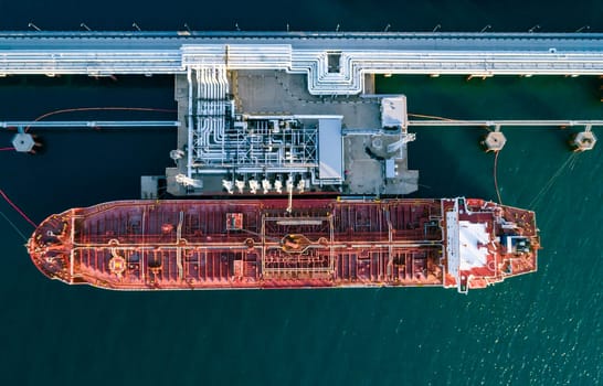 Aerial top down view of a large oil tanker docked at a pier in the port in process of loading.