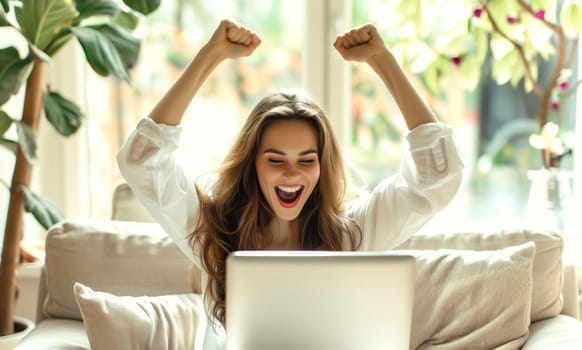 Happy overjoyed laughing woman celebrating success raising her hands up while working on laptop sitting at home office