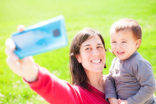 Mother takes a selfie with her son next to a green meadow. Big smile on their faces. Family. 