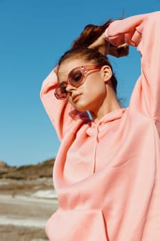 Relaxing beach day woman in pink sweatshirt and sunglasses strikes a pose with hands on head