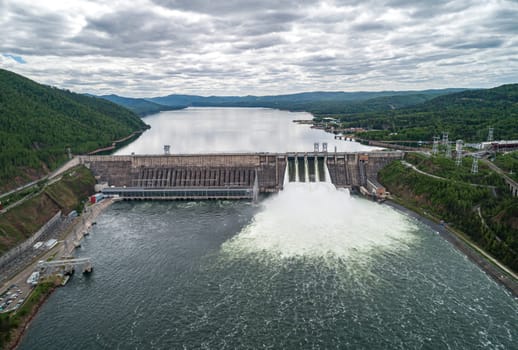 Aerial view of concrete dam releasing water into river on cloudy day. Water discharge at hydroelectric power plant.