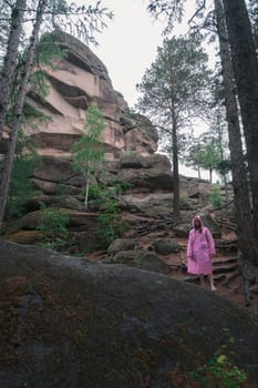 Woman in raincoat in the taiga forest and rocks of the Stolby nature reserve park, Krasnoyarsk, Russia