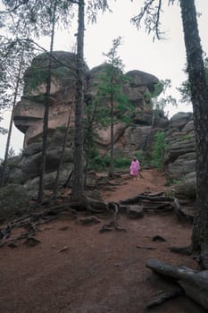 Woman in raincoat in the taiga forest and rocks of the Stolby nature reserve park, Krasnoyarsk, Russia